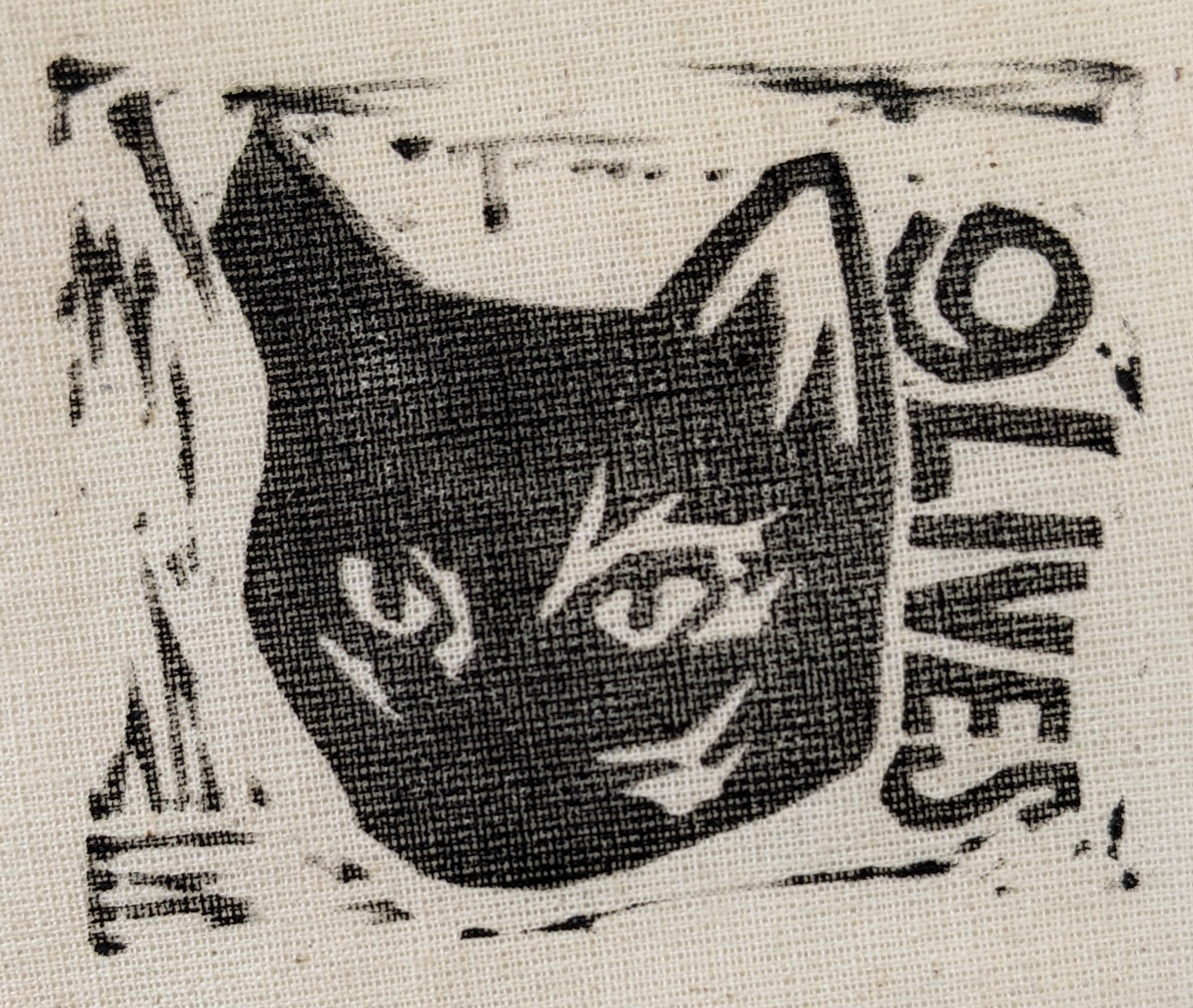 A black lino print on light beige fabric of a black cat's head with printed text beside it reading '9 lives'.